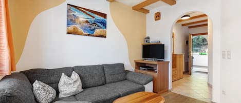 A living room with a grey sofa, a wooden coffee table, a painting on the wall, and a TV stand.