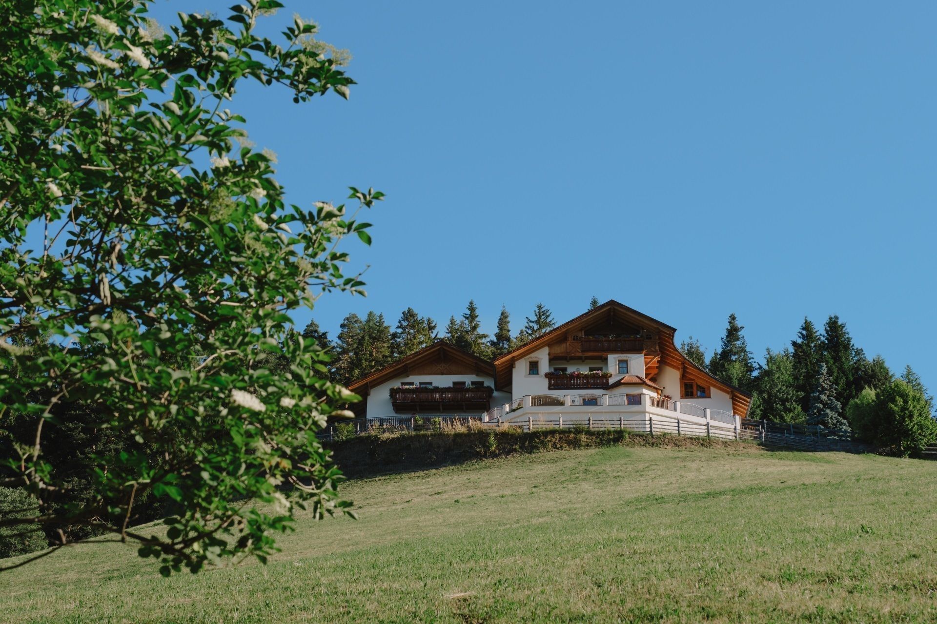 Un chalet à deux étages, doté d’une façade en bois, situé sur une colline verdoyante sous un ciel dégagé.