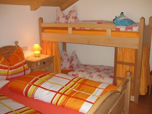 Una cama litera con estructura de madera, una mesita de noche con lámpara y una cama con ropa de cama a rayas.