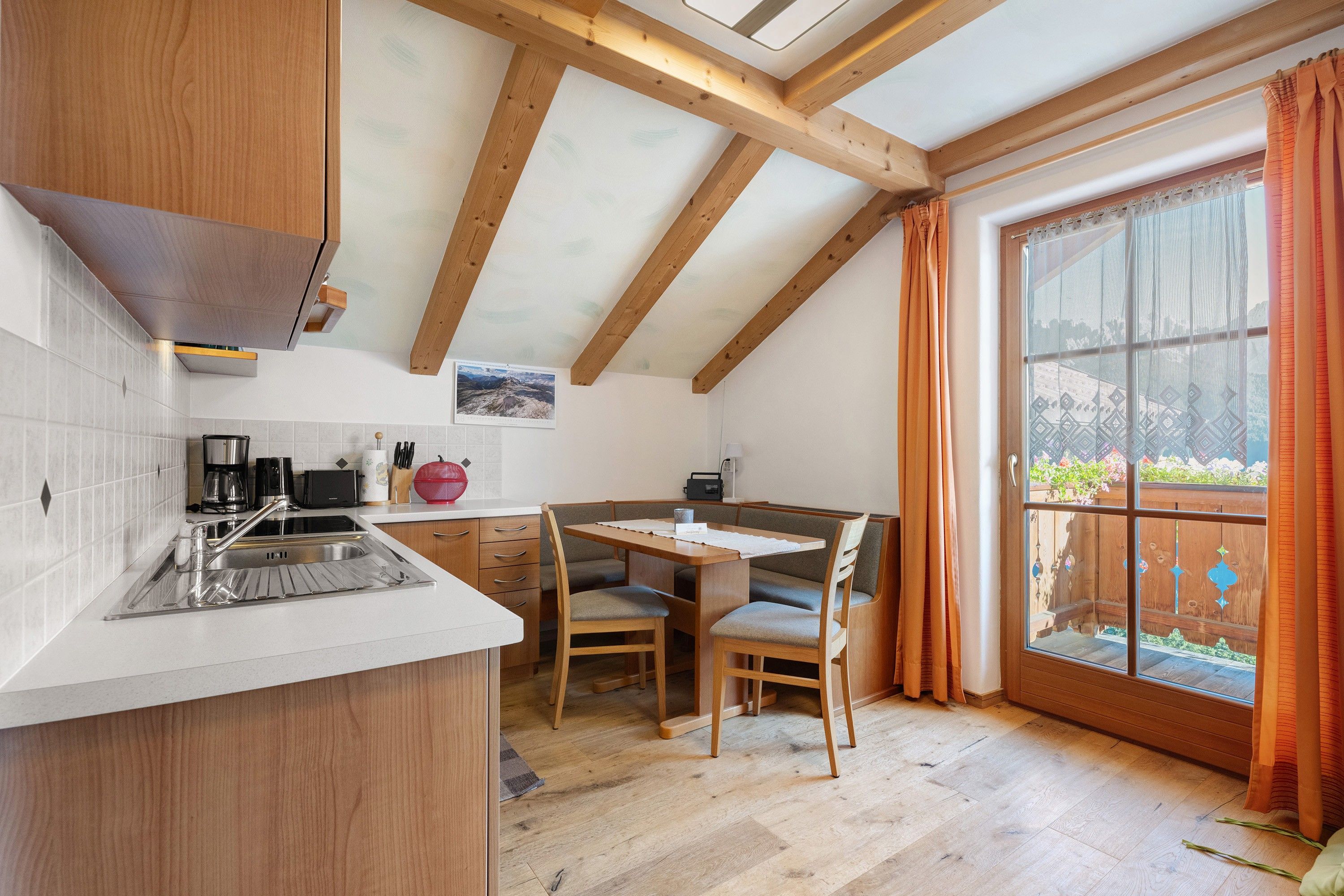 Une cuisine avec un plafond en bois, un coin repas avec une table et des chaises, et une grande fenêtre avec des rideaux.
