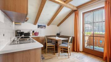 Une cuisine avec un plafond en bois, un coin repas avec une table et des chaises, et une grande fenêtre avec des rideaux.