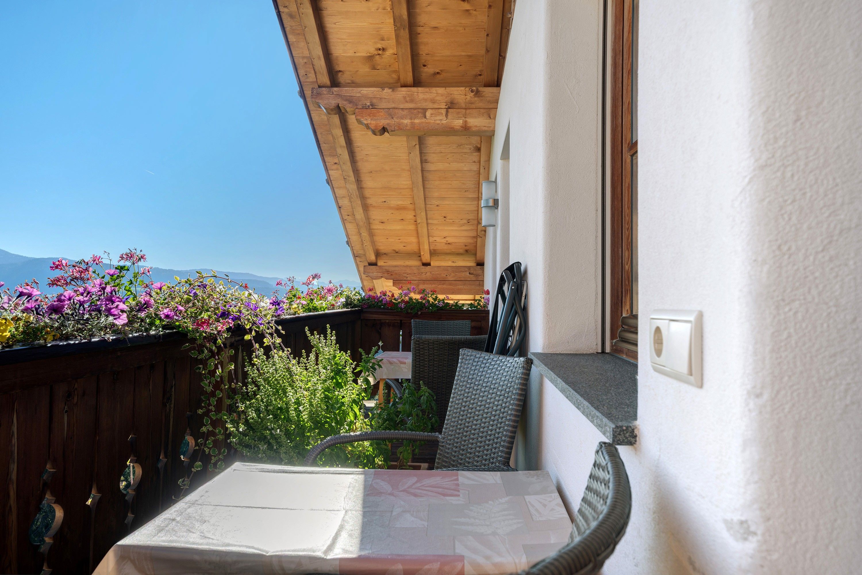 A balcony with a wooden ceiling, a wicker chair, and a table with a white tablecloth.