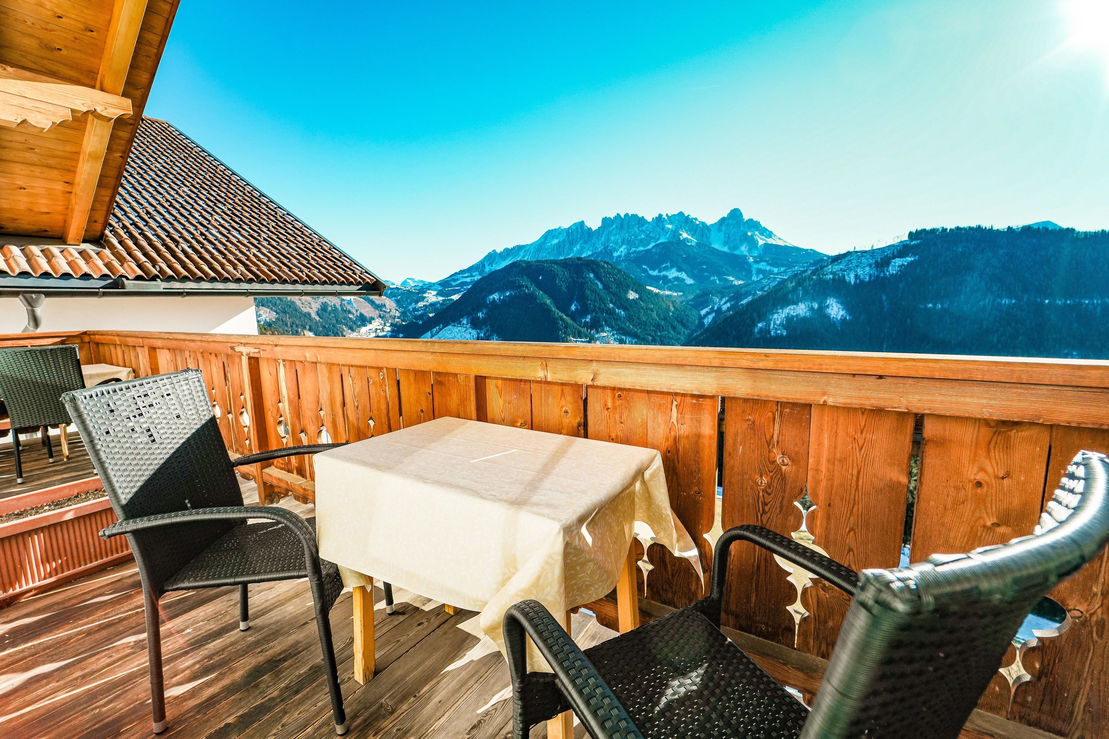 A wooden deck with a table and chairs, overlooking a mountainous landscape.