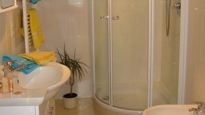 Et badeværelse med bruseniche, håndvask og toiletbøtte.