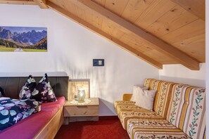 Una habitación con una cama, un sofá, una mesita de noche con lámpara, un cuadro en la pared y techo de madera.