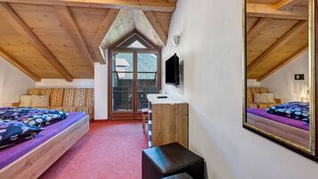 Une chambre avec un plafond en bois, un lit recouvert d’une literie à motifs floraux, un banc et un téléviseur.