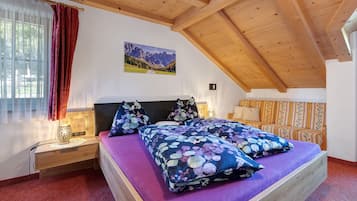 Une chambre avec un plafond en bois, un lit recouvert d’une literie à motifs floraux, une table de chevet avec une lampe et une fenêtre avec des rideaux.