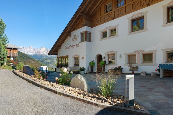 Een traditioneel gebouw in de Alpen met uitzicht op de bergen, houten balken en een bordje dat een restaurant aangeeft.