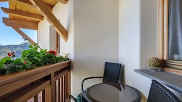 Un balcon avec des balustrades en bois, une chaise en osier, une petite table et un pot de fleurs avec des fleurs rouges.
