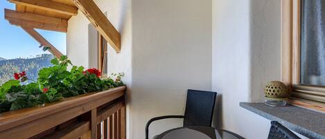 Un balcon avec des balustrades en bois, une chaise en osier, une petite table et un pot de fleurs avec des fleurs rouges.