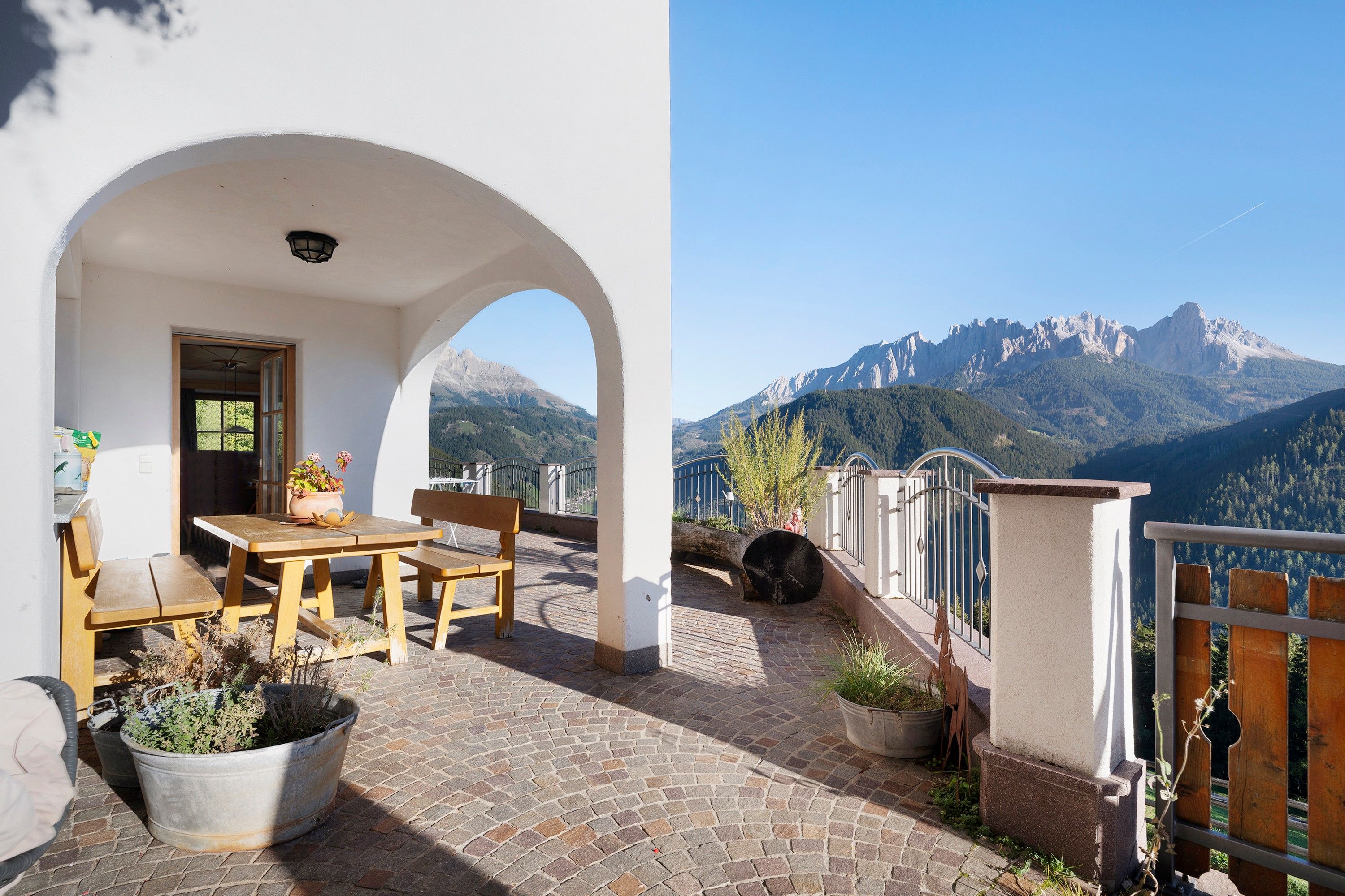 Une terrasse avec une table et des chaises, des plantes en pot et une vue sur les montagnes.