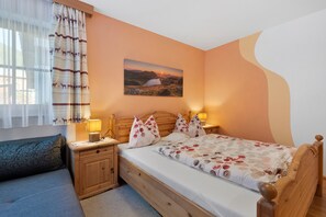 Une chambre à coucher avec un lit en bois, une table de chevet, une lampe, une fenêtre avec des rideaux et un tableau accroché au mur.