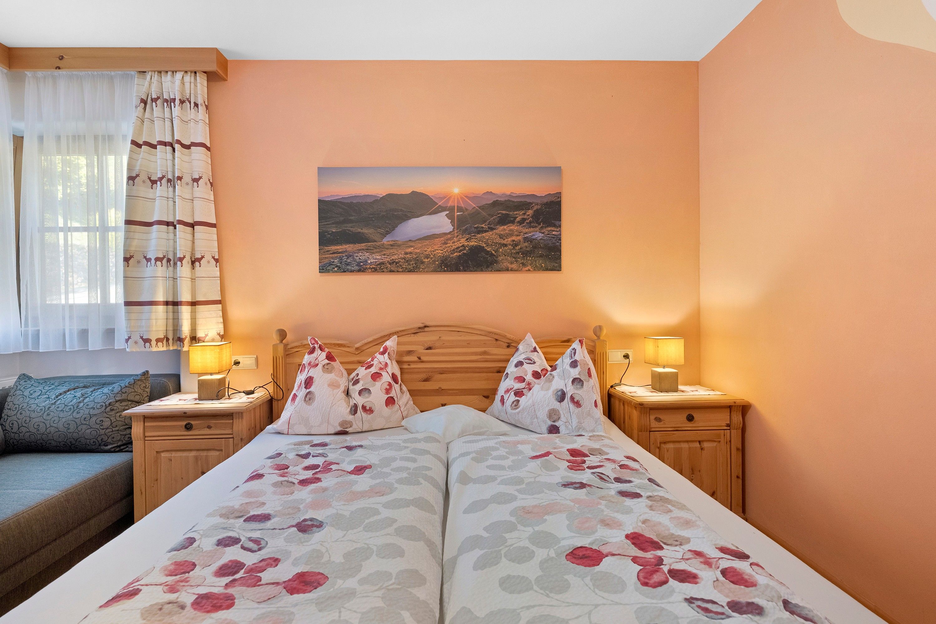 Une chambre à coucher avec un lit, deux tables de chevet avec des lampes, une fenêtre avec des rideaux et un tableau accroché au mur.