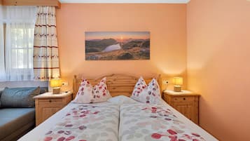 Une chambre à coucher avec un lit, deux tables de chevet avec des lampes, une fenêtre avec des rideaux et un tableau accroché au mur.