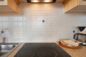 Une cuisine équipée d’une plaque de cuisson intégrée, d’un évier et d’un plan de travail sur lequel se trouvent une bouilloire et une pile de serviettes.