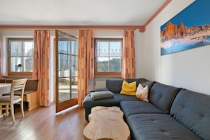 A cozy living room with a sofa, a wooden coffee table, and a dining area with a chair and table. - Apartment "3 Rosengarten" with Mountain View, Shared Garden and Wi-Fi (Nova Levante)