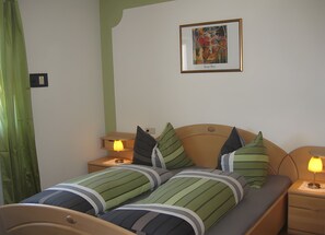 Una cama doble con ropa de cama a rayas, dos lámparas de noche, una obra de arte enmarcada en la pared y una cortina verde.