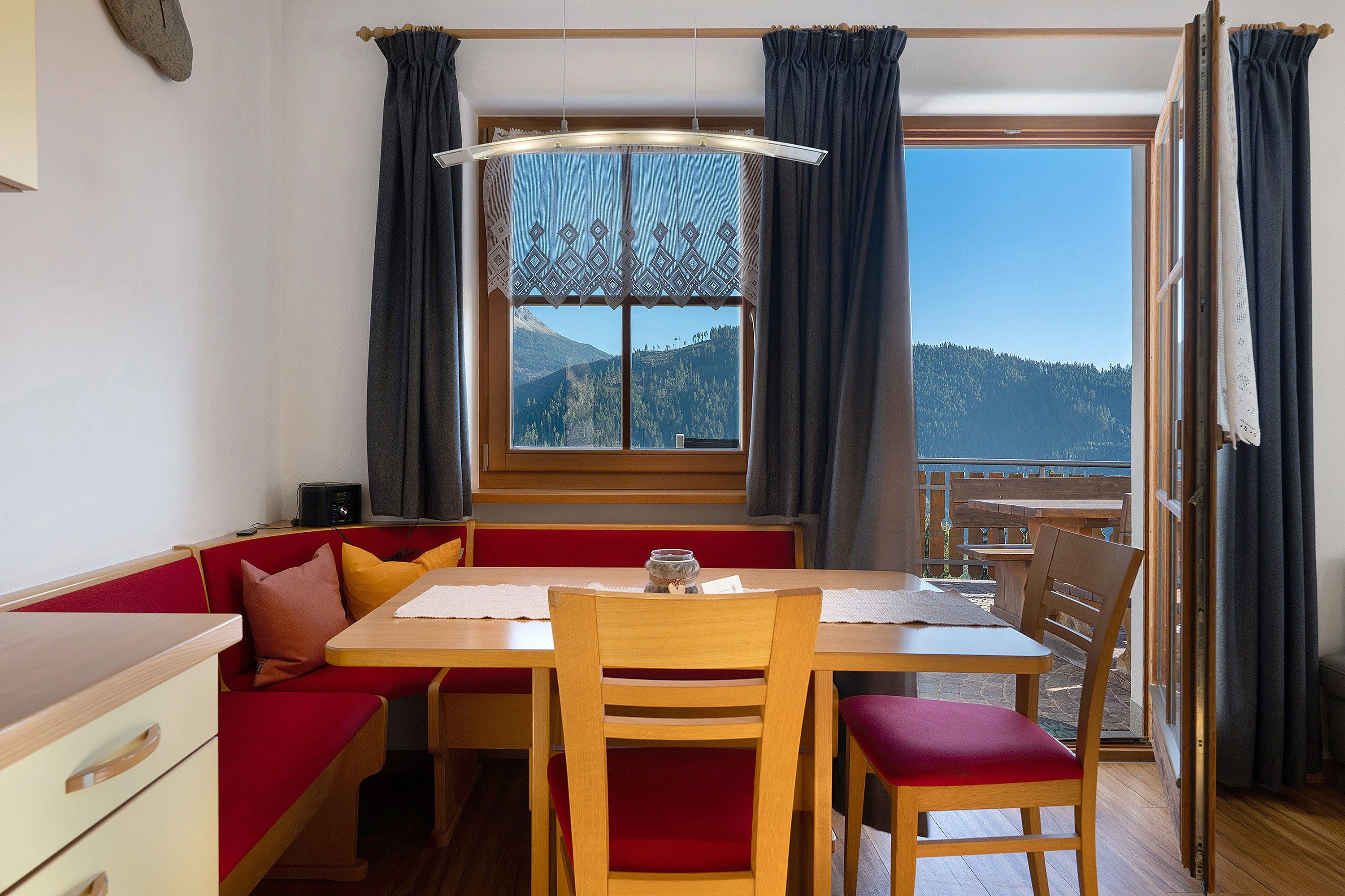 Une pièce chaleureuse avec une table en bois, des sièges rembourrés de couleur rouge, une radio et une vue sur un paysage montagneux par une grande fenêtre.