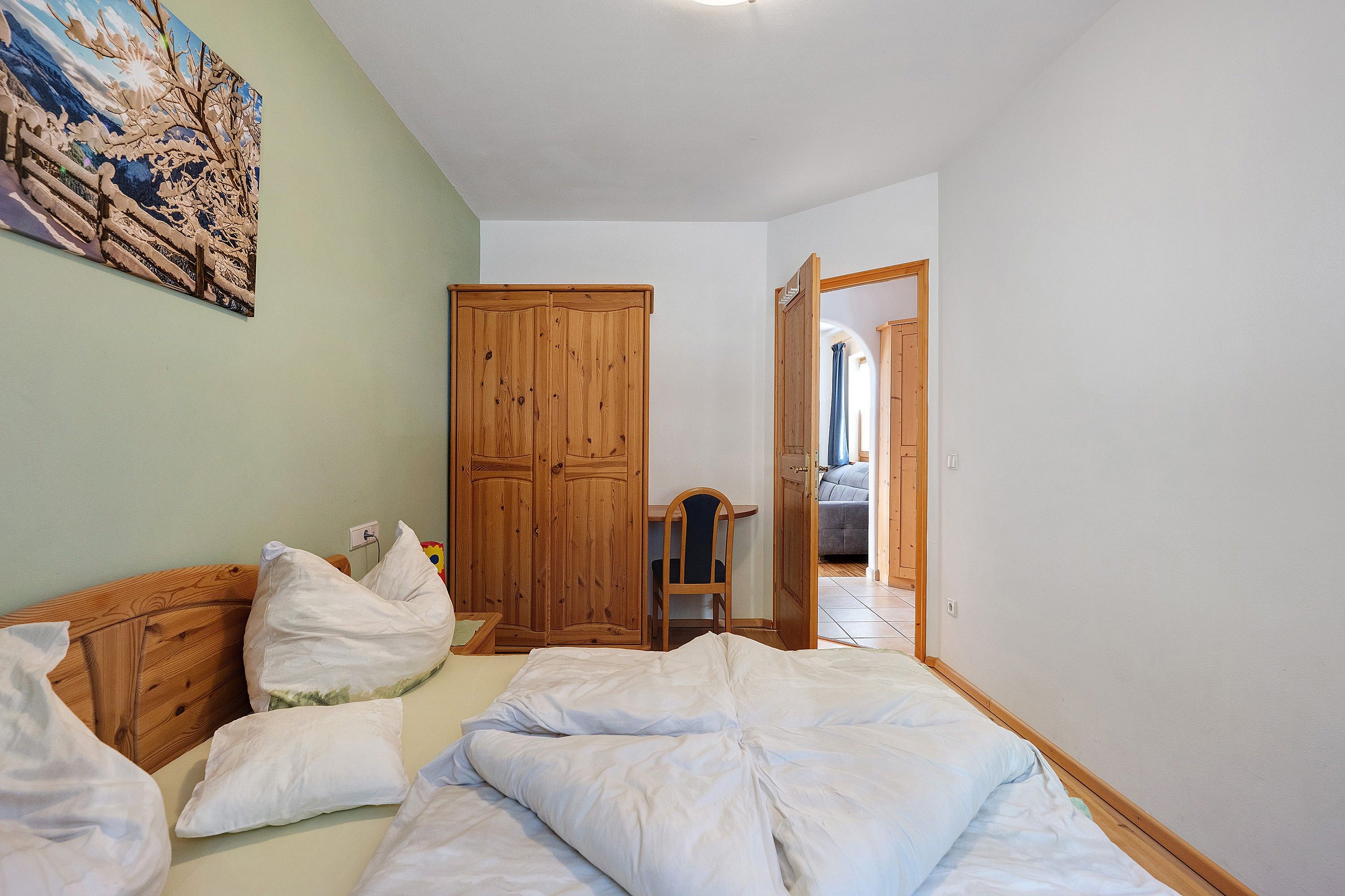 Una camera da letto con un letto, un armadio in legno, una scrivania con una sedia e una porta che dà su un'altra stanza.