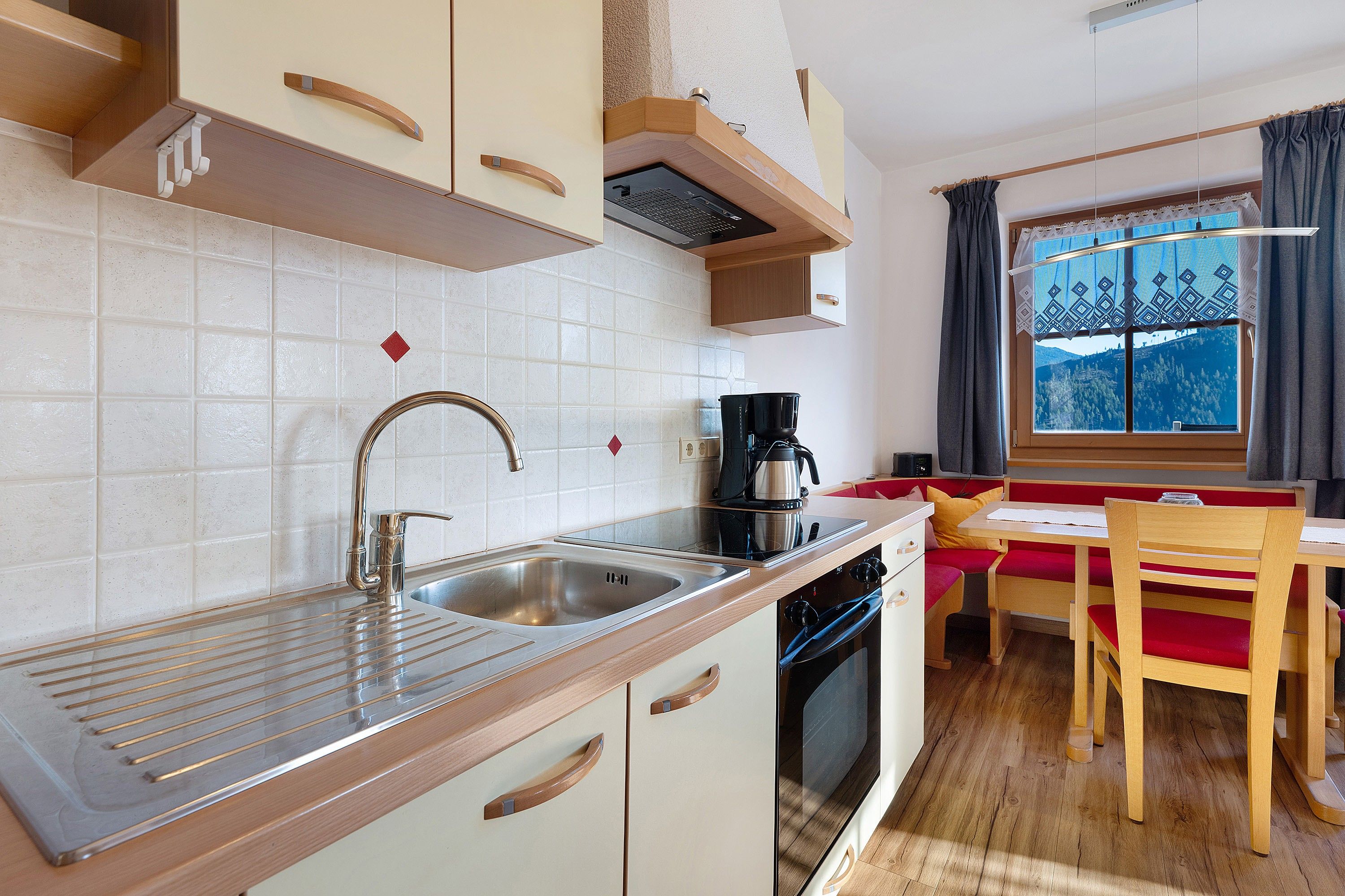 A compact kitchen with a sink, stove, and a window with a view of a mountainous landscape.