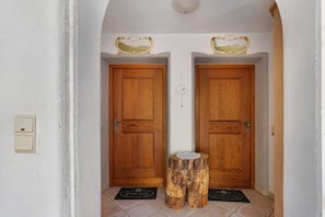 Un pasillo con dos puertas de madera, un interruptor de luz y un felpudo.