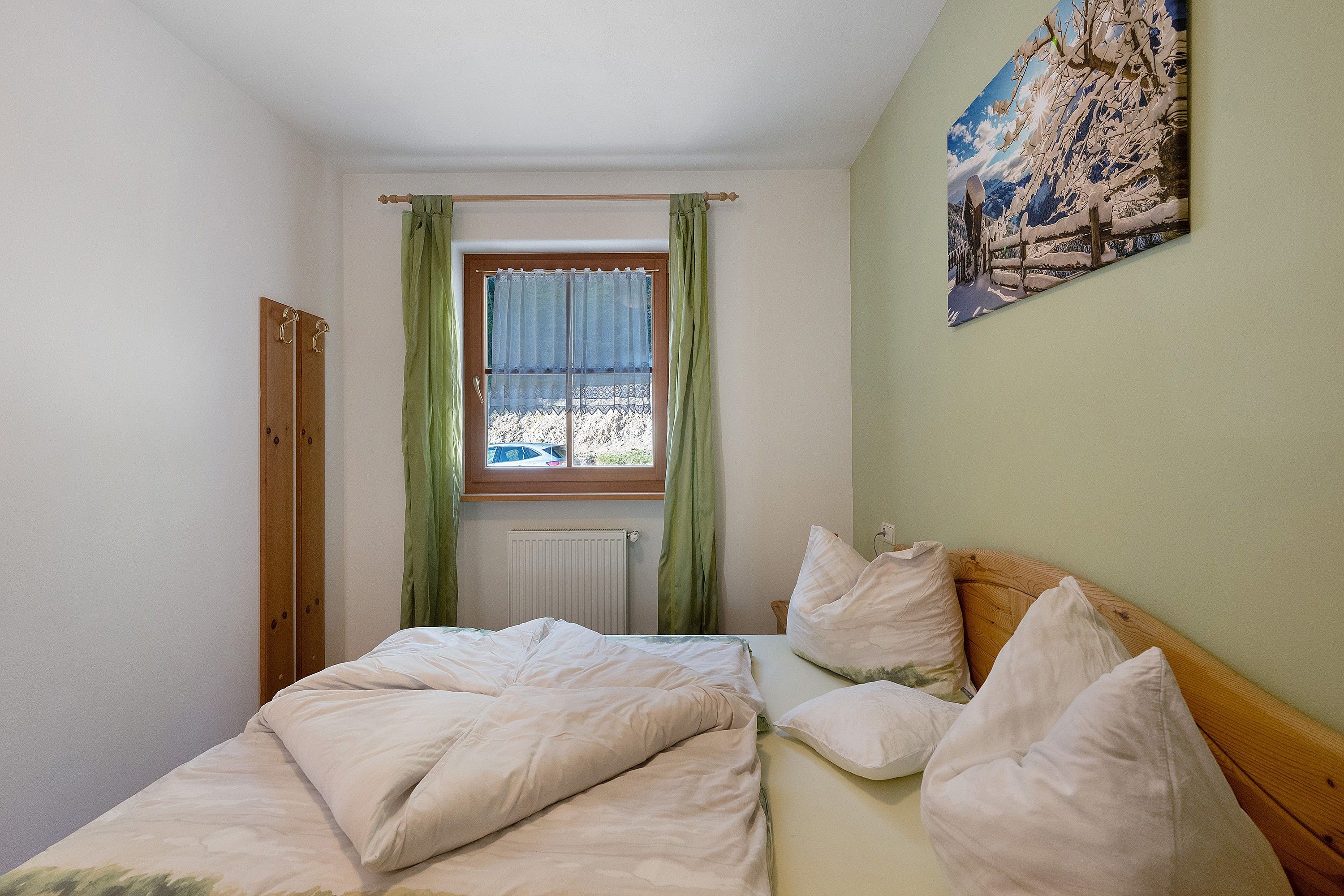 Une chambre à coucher avec un lit, un radiateur, une fenêtre avec des rideaux et un tableau accroché au mur.