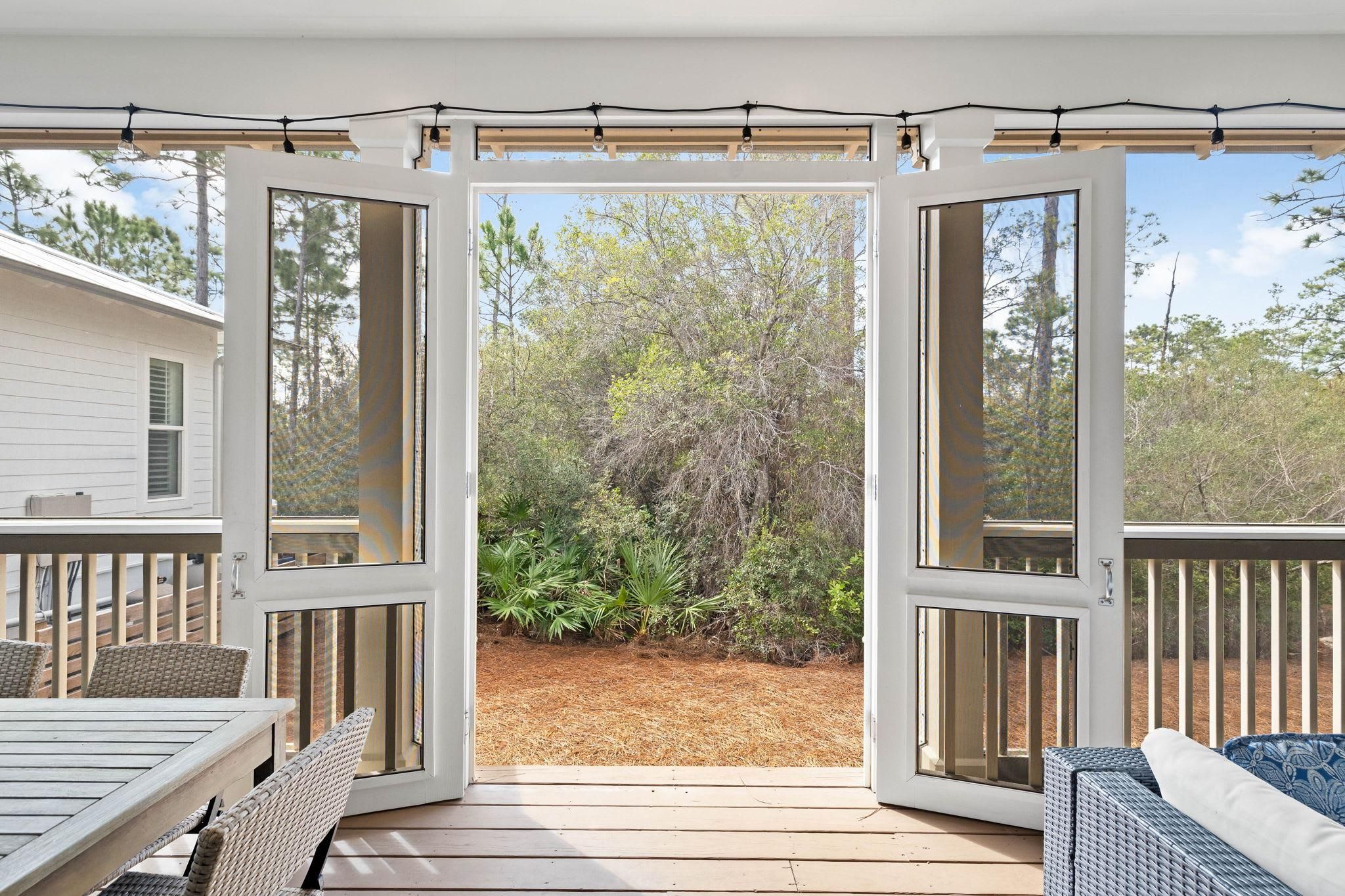 An open deck with a view of a wooded area, a wooden table, and wicker chairs.