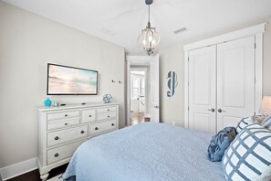 A bedroom with a large bed, a dresser, a television, and a chandelier. - Sea Esta (Santa Rosa Beach)