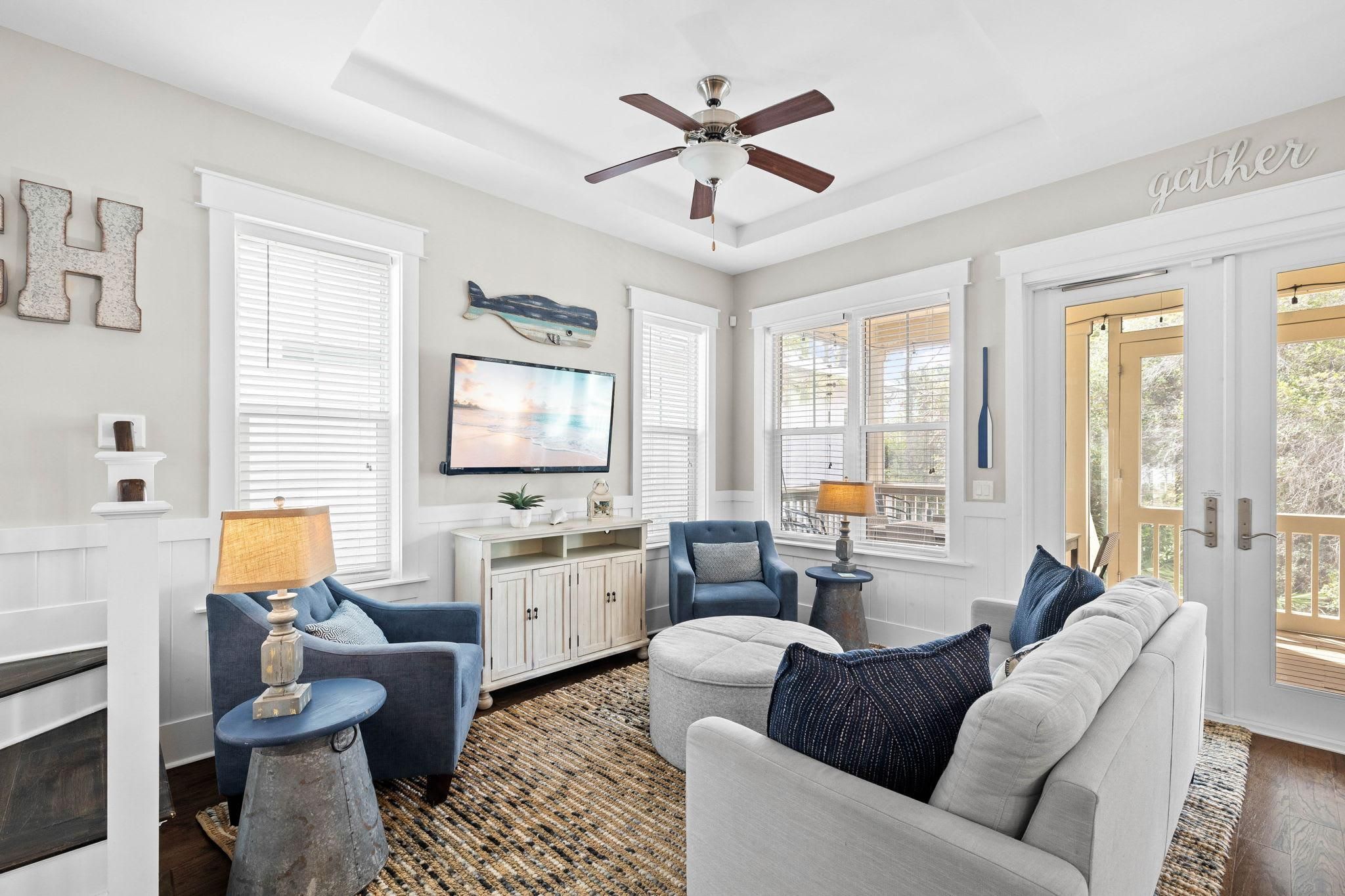 A well-lit living room with a ceiling fan, a television, and a seating area with a sofa and chairs.