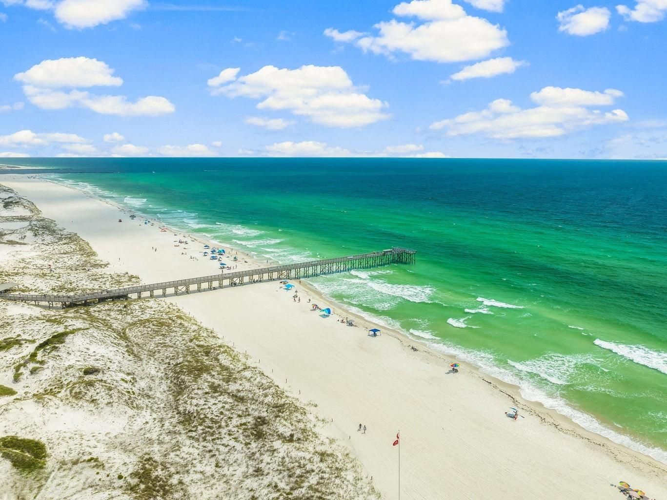 A beach with a pier extending into the ocean, sandy shores, and clear blue water.