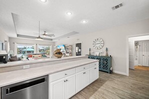 Une cuisine moderne avec un îlot central, des placards intégrés, une horloge au mur et un ventilateur de plafond.