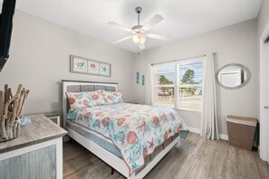 A bedroom with a bed, a ceiling fan, a window with curtains, a bedside table, and a mirror. - Angler Dock House (Panama City Beach)