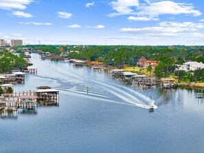 A river with a boat creating a wake, surrounded by docks and buildings. - Angler Dock House (Panama City Beach)