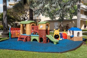 A children's playground with various play structures, surrounded by palm trees and a building in the background. - Top-View Oceanside 2BR Villa, Beachfront Marriott St. Kitts – Dec 8–15, Sleeps 8 (Frigate Bay)
