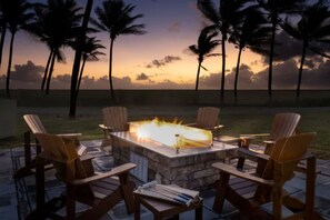 An outdoor seating area with a fire feature, surrounded by chairs, set against a sunset with palm trees. - Top-View Oceanside 2BR Villa, Beachfront Marriott St. Kitts – Dec 8–15, Sleeps 8 (Frigate Bay)