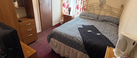 A bedroom with a bed, a wardrobe, a desk with a chair, a bedside table, and a window with curtains.