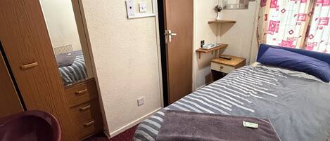 A bedroom with a bed, a wooden wardrobe, a bathroom with a red sink, and a mirror.