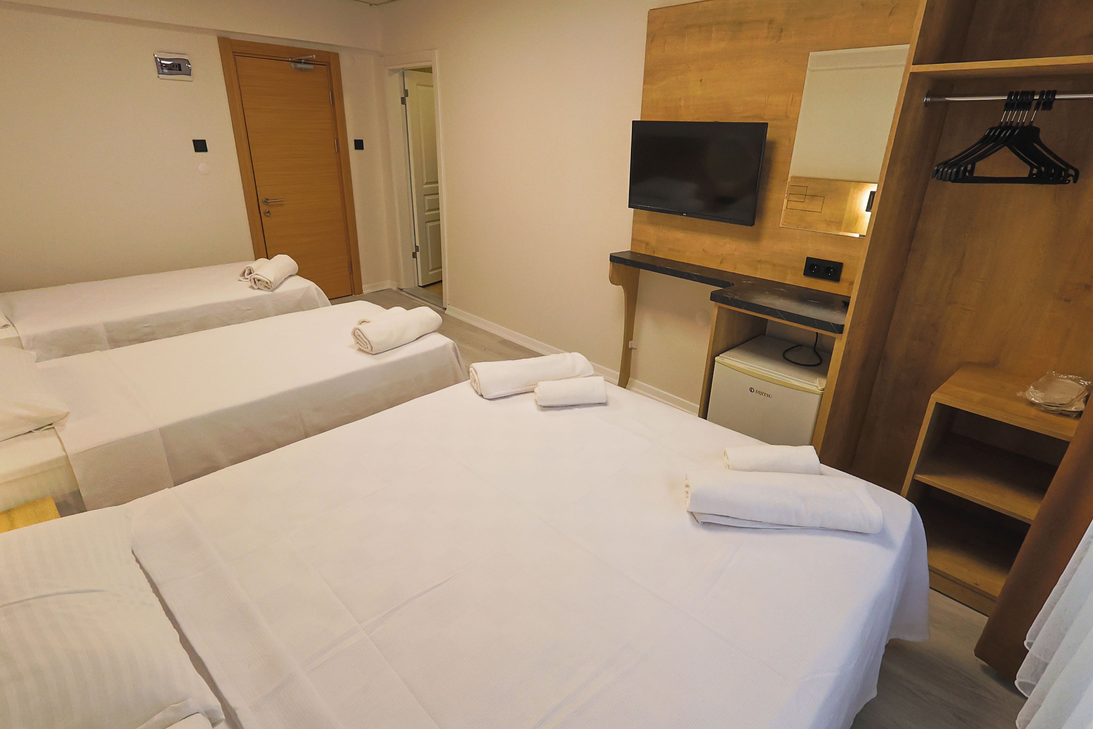 Una habitación de hotel con dos camas individuales, un televisor montado en un panel de madera y un armario de madera con espejo.