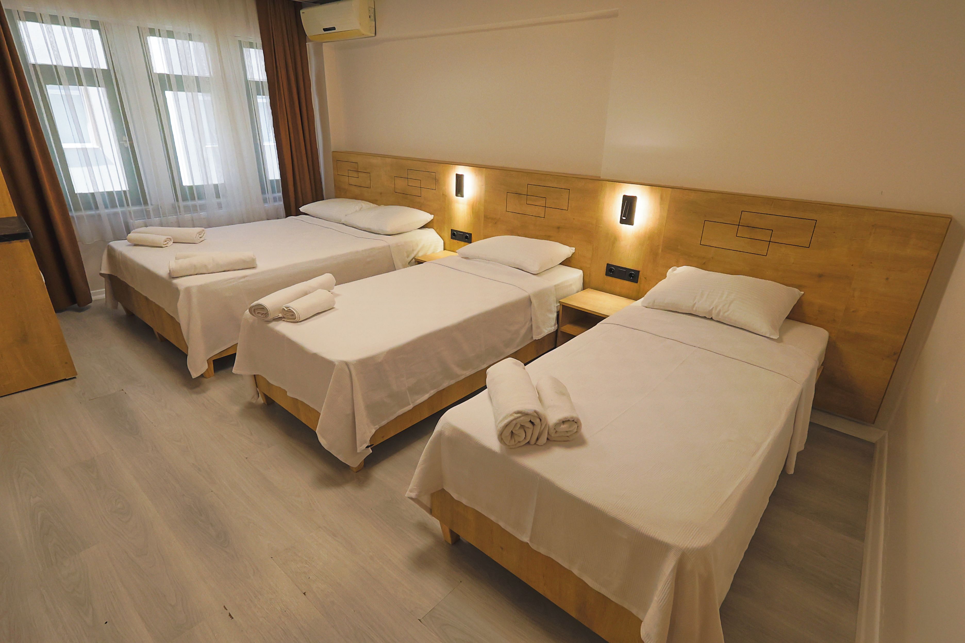 Quarto de hotel com três camas de solteiro, cada uma com toalha dobrada, cabeceiras de madeira e luminárias de cabeceira.