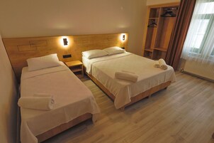 Habitación de hotel con dos camas, cabecera de madera, lámparas de noche, un armario y una ventana con cortinas.