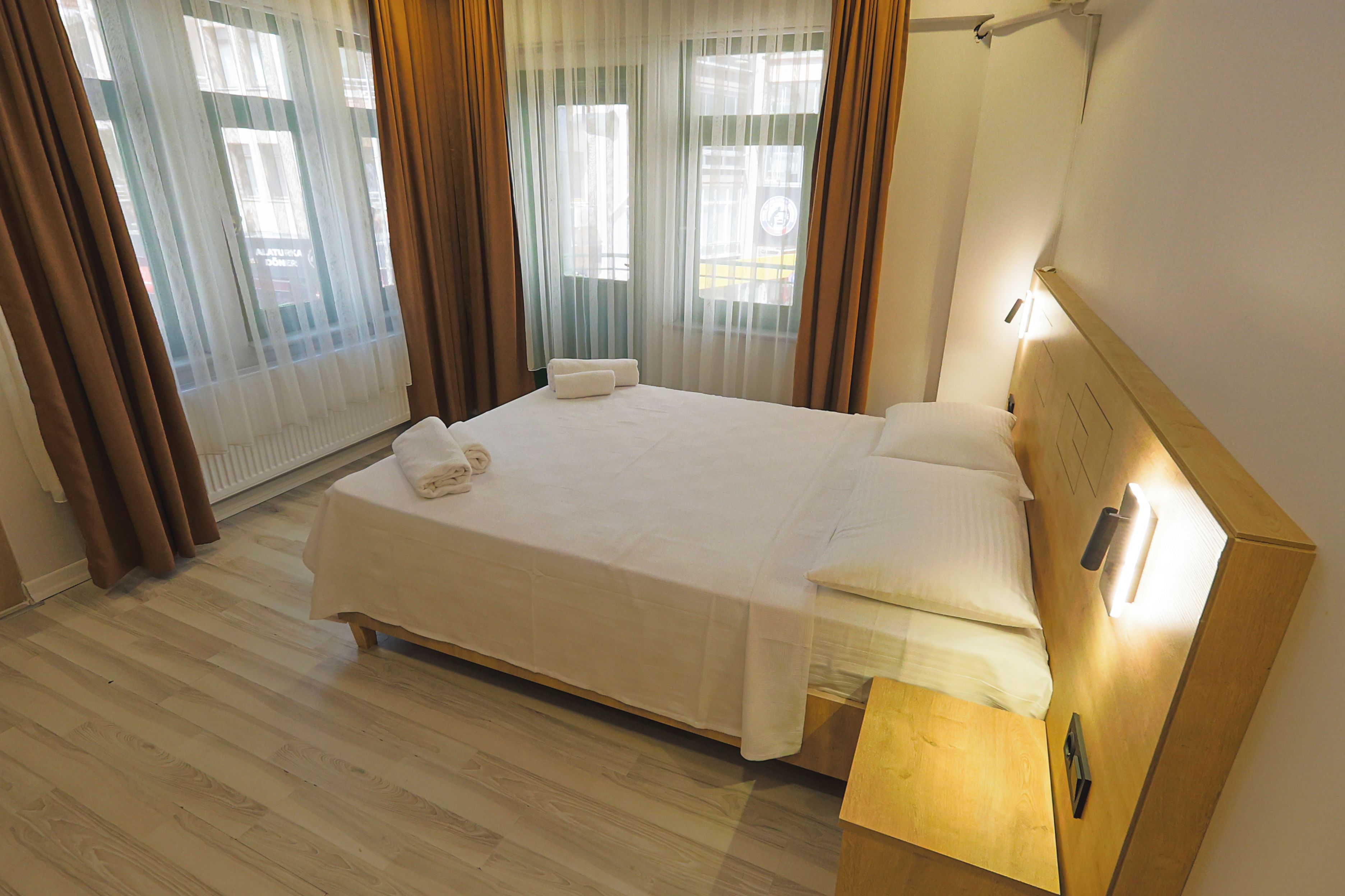 Une chambre d’hôtel avec un lit, des rideaux, une tête de lit en bois et une table de chevet.