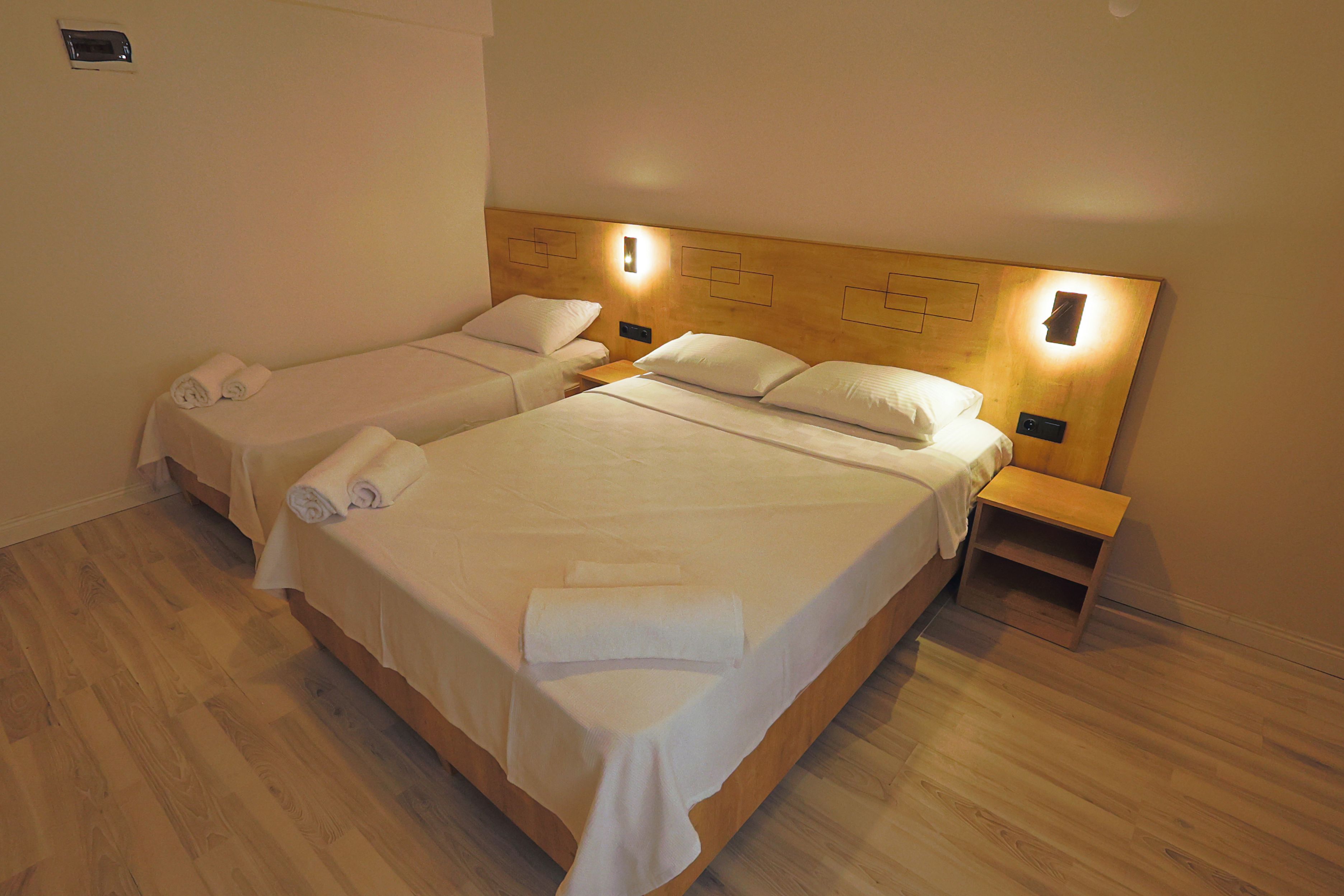 Quarto de hotel com duas camas de solteiro, cabeceiras de madeira, mesas de cabeceira e toalhas dobradas com cuidado.