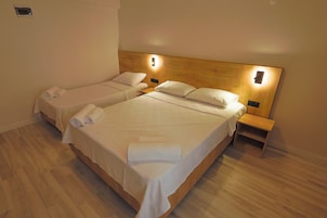 Quarto de hotel com duas camas de solteiro, cabeceiras de madeira, mesas de cabeceira e toalhas dobradas com cuidado.