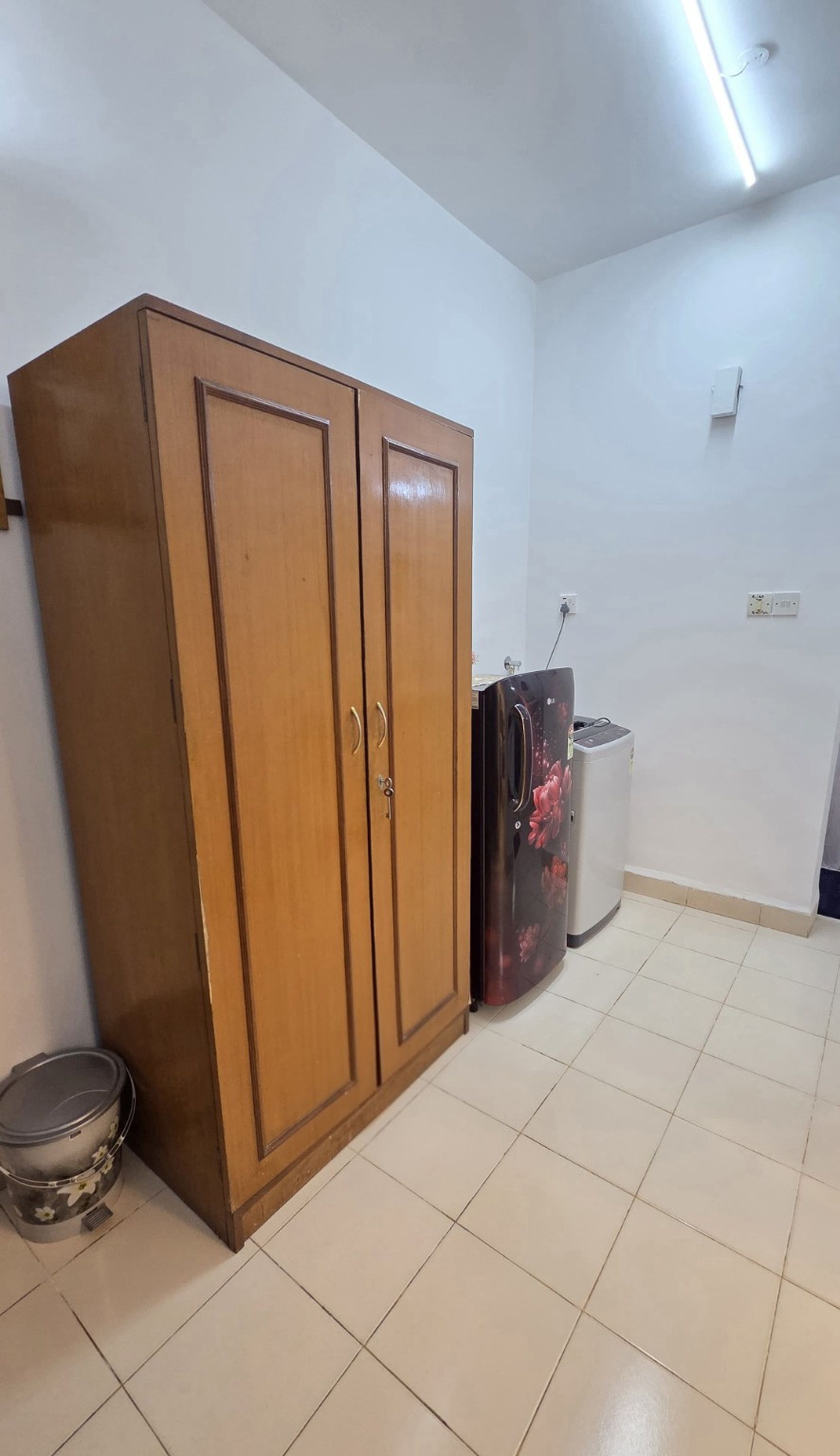 Ein Zimmer mit einem Holzschrank, einer Mülleimer und einem Kühlschrank.