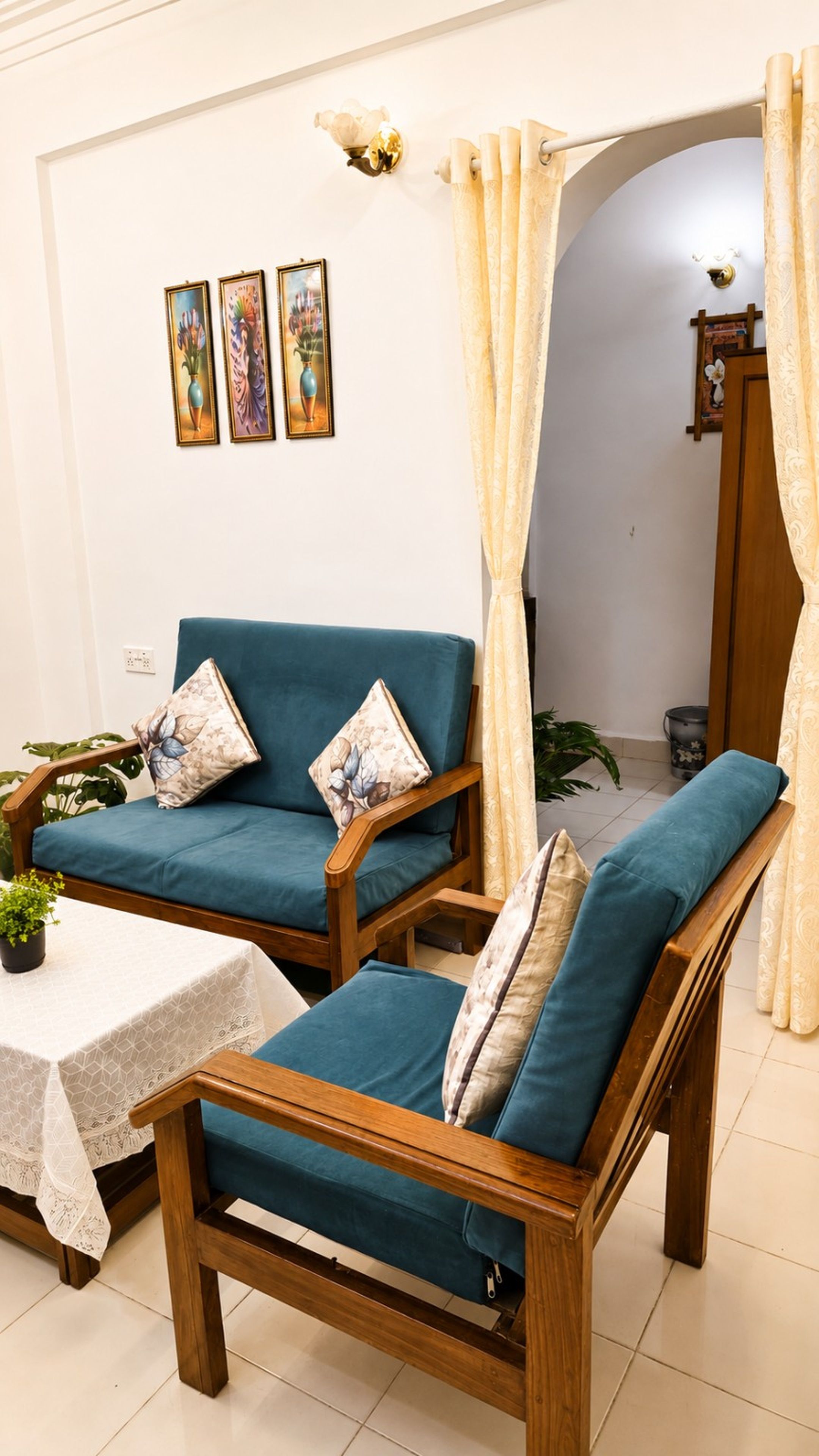 Una habitación con dos sillas de madera con cojines azules, una mesita con mantel blanco y una pared con tres cuadros enmarcados.