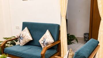 Una habitación con dos sillas de madera con cojines azules, una mesita con mantel blanco y una pared con tres cuadros enmarcados.
