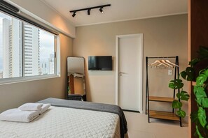 A bedroom with a bed, a TV, a mirror, a wardrobe, and a window with a city view. - BNB Flex Premium (Recife)