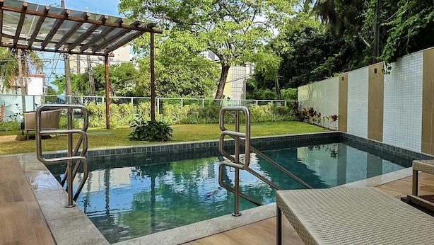 A swimming pool with metal railings, a covered seating area, and a tiled wall. - BNB Flex Premium (Recife)