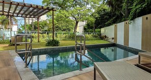 A swimming pool with metal railings, a covered seating area, and a garden with grass and plants. - BNB Flex Premium (Recife)