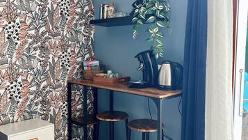 Een kleine, knusse kamer met behang met een patroon, een bureau met een waterkoker, en een potplant.
